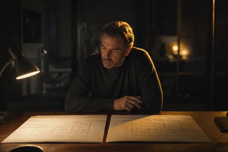 An owner comparing two sets of building plans on a table under one lamp