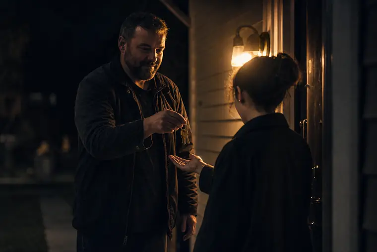 A landlord handing keys to a tenant at the door of a small duplex